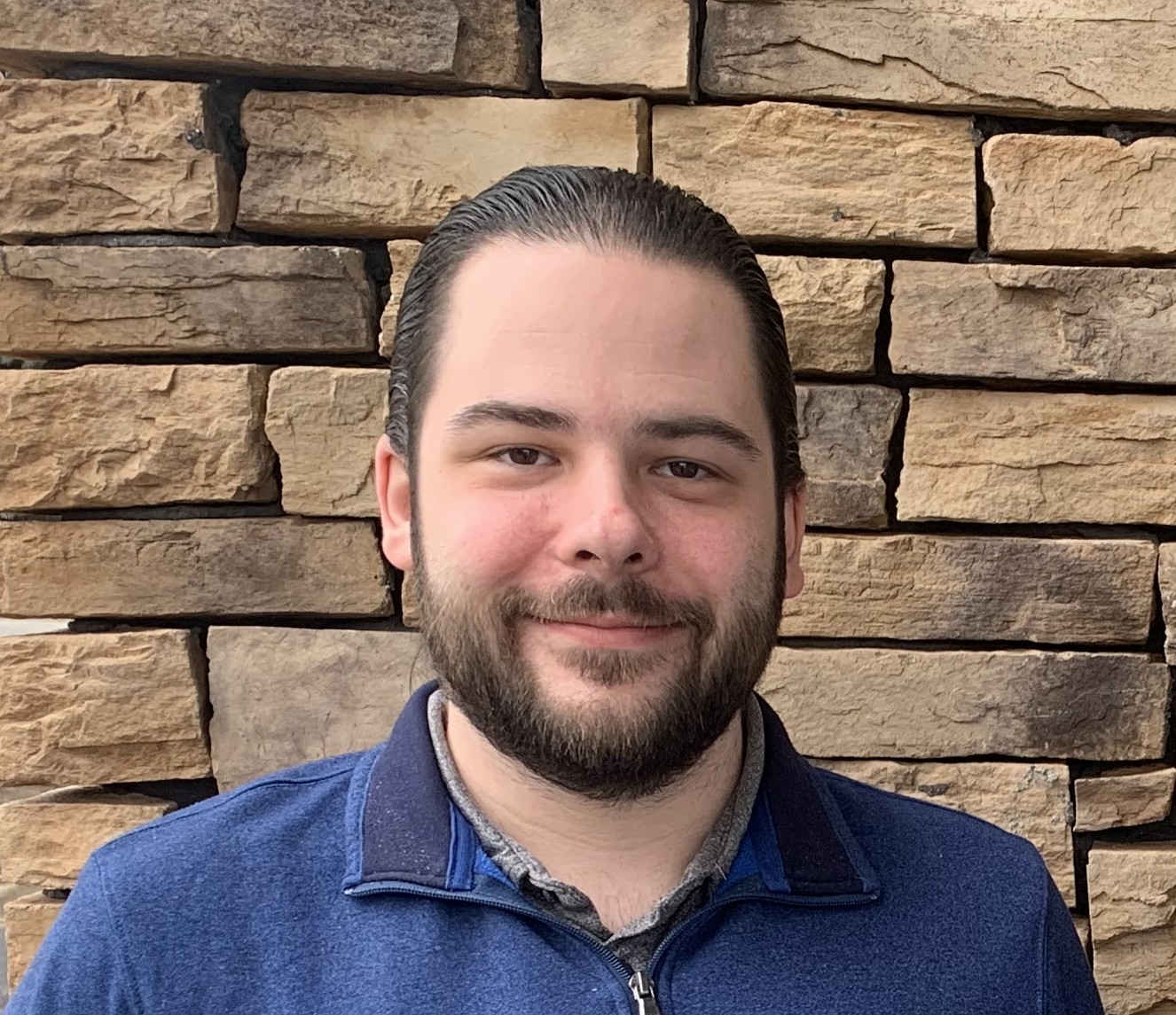 Ethan Bowman, Regional Planner at the Commonwealth Regional Council, smiling in front of a stone wall background.