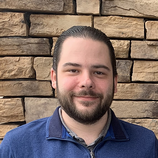 Ethan Bowman, Regional Planner at the Commonwealth Regional Council, smiling in front of a stone wall background.
